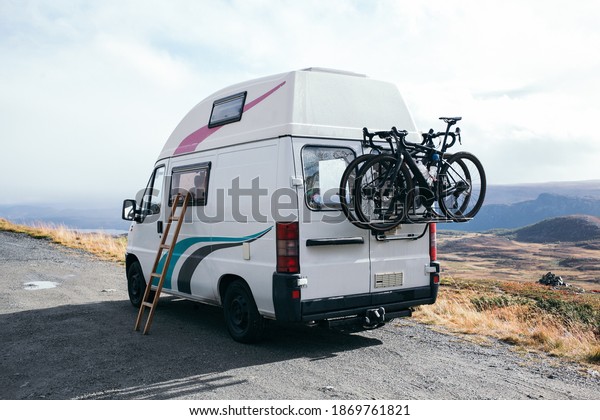 Amazing vintage camper van parked on\
gravel wild camping spot. Two bikes attached to bike rack in the\
back. Sleeping on top of car. Vanlife adventures\
concept