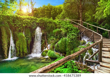 Amazing waterfall in Plitvice Lakes National Park, Croatia, Europe. Majestic view with turquoise water, wooden handrail stairs, and sunset sunny beams, travel destinations background