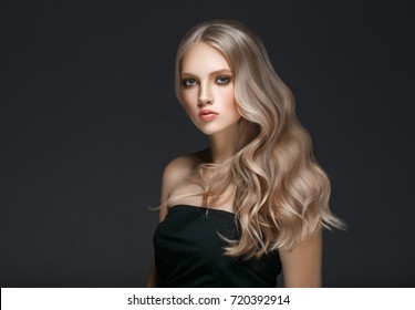 Amazing woman portrait. Beautiful girl with long wavy hair. Blonde model with hairstyle over black background