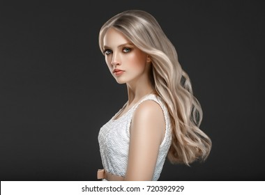 Amazing woman portrait. Beautiful girl with long wavy hair. Blonde model with hairstyle over black background