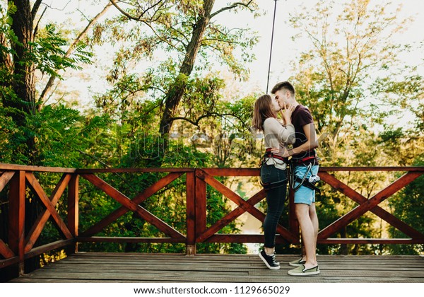 Amazing young couple embracing and kissing on a\
wooden platform in the trees before ziplining on rope slide through\
forest.