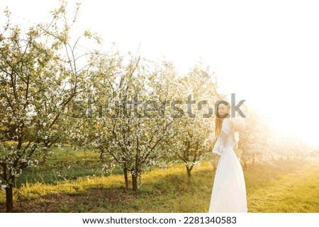 Amazing young woman in a straw hat posing in a garden of flowering trees in spring.