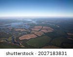 The Amazon river and jungle form very high in the air. Aerial view of the blue water river flowing across the tropical rainforest, cropland and plantations.