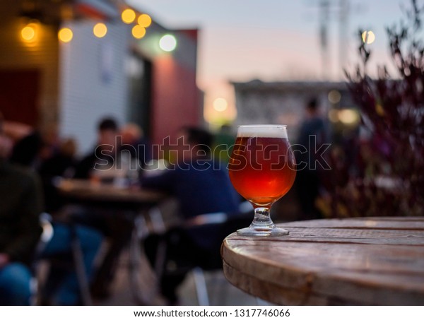 amber beer in tulip glass, craft beer on the\
patio, patio table with beer, patio lights, microbrewery, people in\
the background