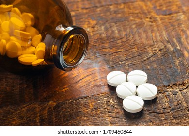 An amber bottle full of aspirin pills with some pills outside on a wood table.