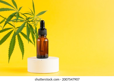Amber glass cosmetic bottles with CBD oil and hemp leaves stand on the podium. Cosmetics CBD oil on a yellow background. Copy space for text.
