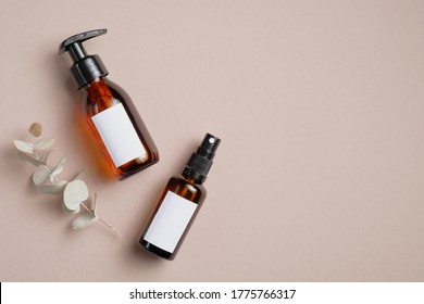 Amber glass cosmetic bottles and eucalyptus leaves on brown background. SPA bathroom natural cosmetic packaging mockup. Flat lay, top view. 