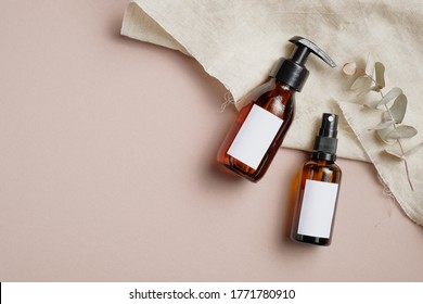 Amber Glass Cosmetic Bottles Set With Towel And Eucalyptus Leaves On Beige Background. Beauty Products Packaging Mockups With Blank White Labels. Skin Care Concept.