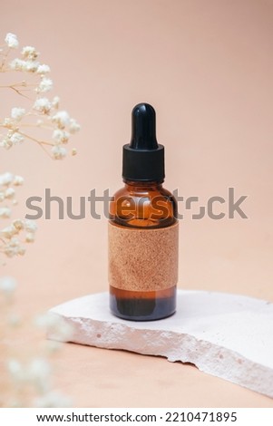 Amber glass dropper bottle with craft label filled serum or essential oil. Beige background with daylight with beautiful flowers. Skincare natural cosmetic. Beauty concept for face and body care