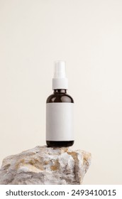 Amber glass spray bottle with blank white label standing on a rock. Cosmetic bottle mockup.