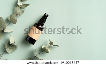 Amber glass spray cosmetic bottle and eucalyptus leaves on green background. SPA herbal beauty product packaging design, branding.