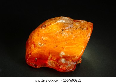 Amber. A Piece Of Natural Mineral From An Ancient Fossil Resin On A Black Background. Sunstone. Fashionable Material For Jewelry. Colored Stone. Crystal. Glowing Object. Vintage. Pitch