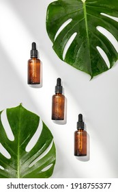Amber serum cosmetic bottles and tropical leaves on white background, flat lay, top view