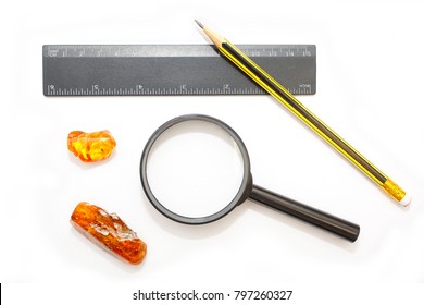 Amber. A set of tools for studying amber. Ruler, pencil, magnifying glass and pieces of amber on a white background. The tools of scientists for amber research.Sunstone and composition of instruments.