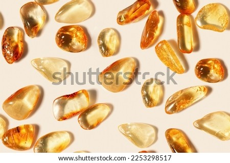 Amber stones on light beige background, minimal monochrome seamless pattern, transparent stone yellow beige color. Natural gemstone mineral. Top view Amber textured fon. Nature gems at sunlight