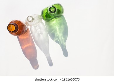 An Amber, A White And A Green Bottle On A White Background While Its Shadow Is Reflected On The Background