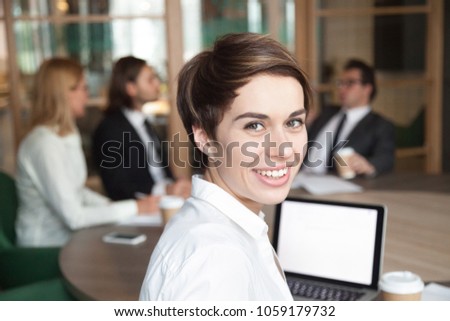 Ambitious attractive smiling young businesswoman looking at camera at group meeting, happy executive manager, team leader, successful professional interpreter or business coach head shot portrait