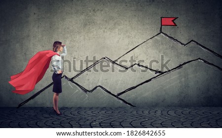 Ambitious business woman looking at the top of the mountain with red flag