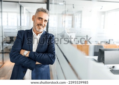 Ambitious mature male entrepreneur ceo manager in formal wear stands in contemporary office space, leaned on glass partition, smiling 50s mature businessman looks at camera