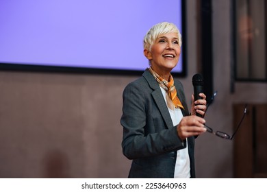 Ambitious senior woman giving a speech. standing at the projection screen, holding glasses. - Powered by Shutterstock