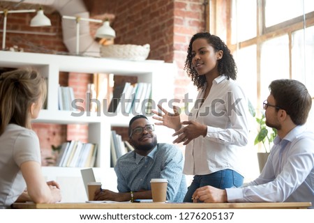 Ambitious smart african black female employee speaking at diverse meeting share creative idea opinion at group briefing while jealous envious skeptical male coworkers looking listening to colleague Foto stock © 