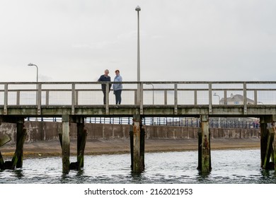 Amble, Northumberland, UK - May 22nd, 2022: Two People Standing On A Pier Enjoying The Sea View.