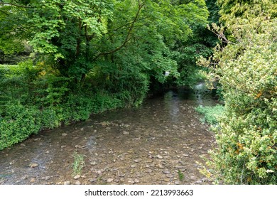 The Ambling Bybrook River Flowing Through Castle Combe In A Wooded Cotswold Valley