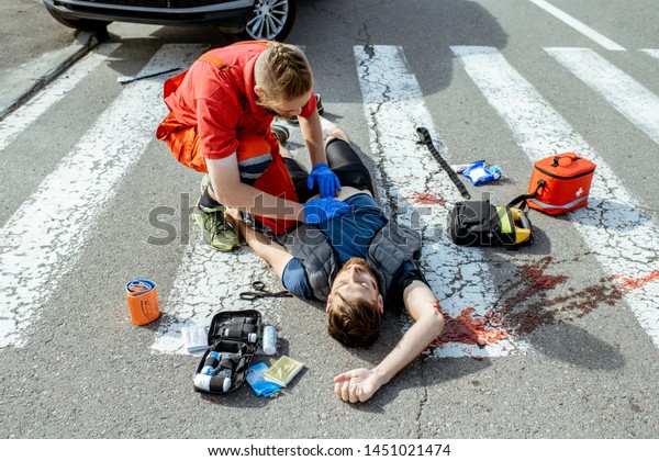 Ambluence\
worker applying emergency care to the injured bleeding man lying on\
the pedestrian crossing after the road\
accident