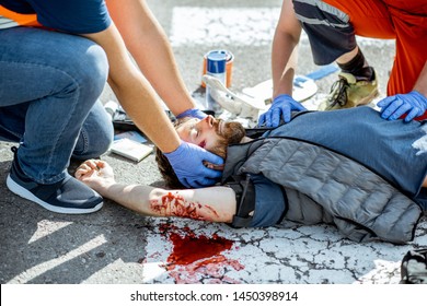 Ambluence workers applying emergency care to the injured bleeding man lying on the pedestrian crossing after the road accident