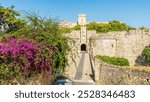 Amboise Gate in Rhodes showcases a striking mix of medieval architecture and natural beauty, with stone fortress walls and vibrant flowers, perfect for historical tourism.