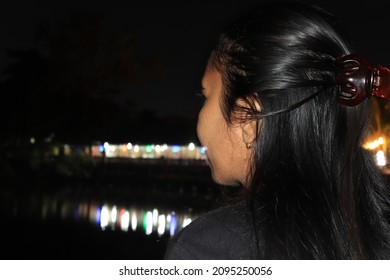 Ambon City-17 December 2021. At Night Beside The Cafe, Accompanied By The Light Reflected From The Seaside, A Woman Sits Looking Forward And Pensive