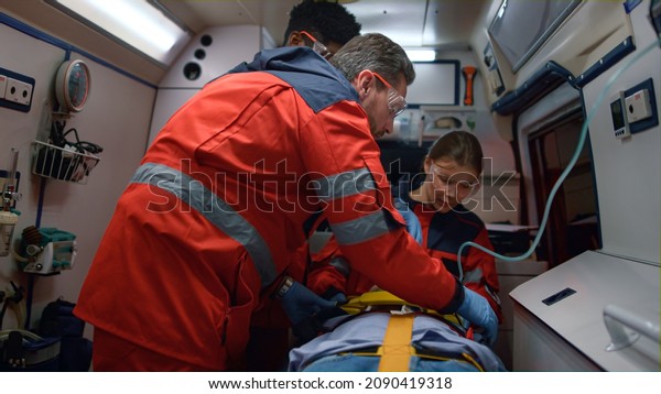 Ambulance doctors saving life of victim in\
ambulance vehicle. Medical team fixing man on stretchers. Mixed\
race paramedics putting oxygen mask on injured patient at way to\
hospital. Healthcare\
concept