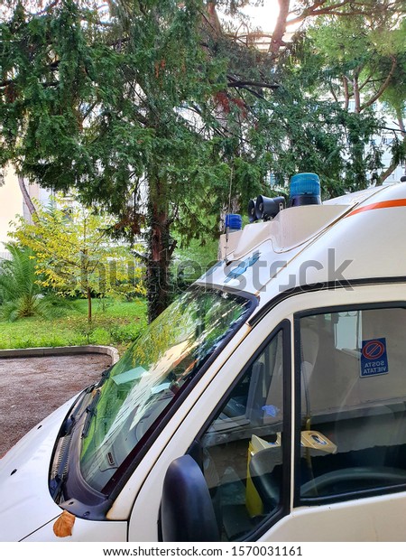 ambulance\
flashing lights parked in the hospital area with nearby trees and\
with no medical health operator on\
board