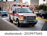 An ambulance with lights activated and a police car behind it  in an urban environment  