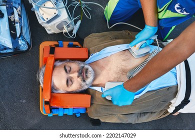 Ambulance paramedic using defibrillator performing cardiopulmonary resuscitation on casualty. First aid for injured mature man lying on emergency stretcher, top view - Powered by Shutterstock