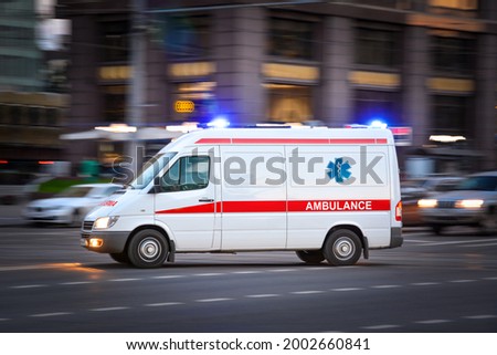 Ambulance Van on a wide city street. White emergency vehicle with warning lights and siren moving fast an avenue. Metropolis rescue services transport. Motion blur and selected focus