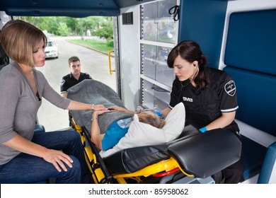 Ambulance Workers Caring For A Senior Woman With Young Caregiver At Side