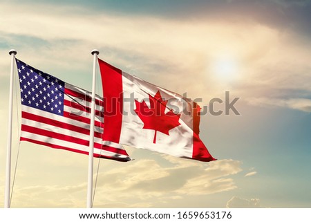 America and Canada national flag cloth fabric waving on the sky with beautiful sun light - Image