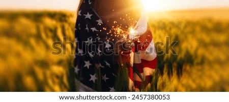 America celebrate 4th of July. Independence Day. Young woman holding bengal fire with American flag at sunset.