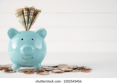 America dollars banknotes money into pastel blue piggy bank and coins on white wooden background. Saving money wealth and financial concept. - Shutterstock ID 1502543456