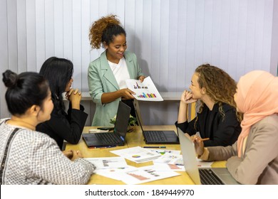 An American African Business Lady Is Presenting Her Project To Other Coworkers. Business Women From Different Ethnic Races And Cultures Working Together In An Office For Business Development Or Plan