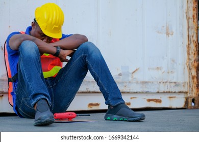 American African Engineer Or Technician Worker Man Sit Close To Cargo Container And He Look Tired And Sleepy Or Lost Job. Concept Of Good System And Manager Support For Better Industrial Business.