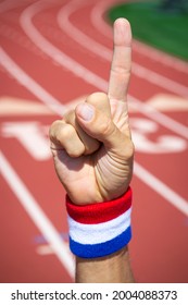 American athlete pointing up in praise with USA red, white, and blue colors wristband in front of a sports track background