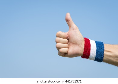 American athlete wearing USA colors red, white, and blue wristband holding thumbs up against blue sky