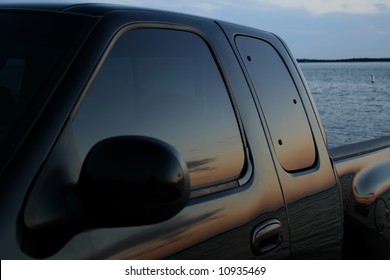 American Black Truck Parked At The Beach With A Sunset Reflection In The Tinted Window