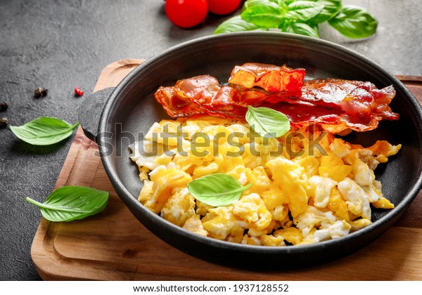American breakfast with scrambled eggs and\
roasted bacon on dark\
background.