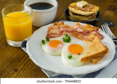 American Breakfast With Sunny Side Up Eggs, Bacon, Toast, Pancakes, Coffee And Juice