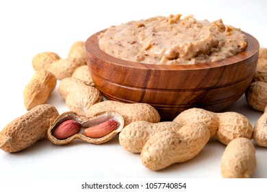 American Breakfast, Sweet Food And Snack High In Calories Concept With A Bowl Of Crunchy Peanut Butter Surrounded By Peanuts Still In Shell, Isolated On White Background