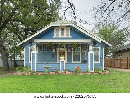 American bungalow style blue house whit well kept front yard.