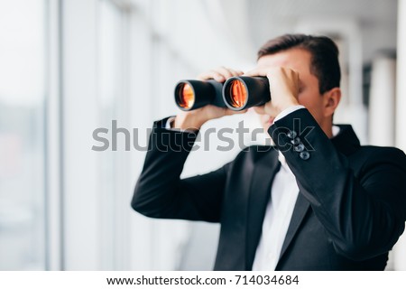 american businessman using binoculars in window office